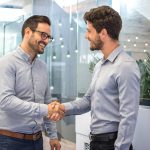Two smiling business men shaking hands together after successful meeting.